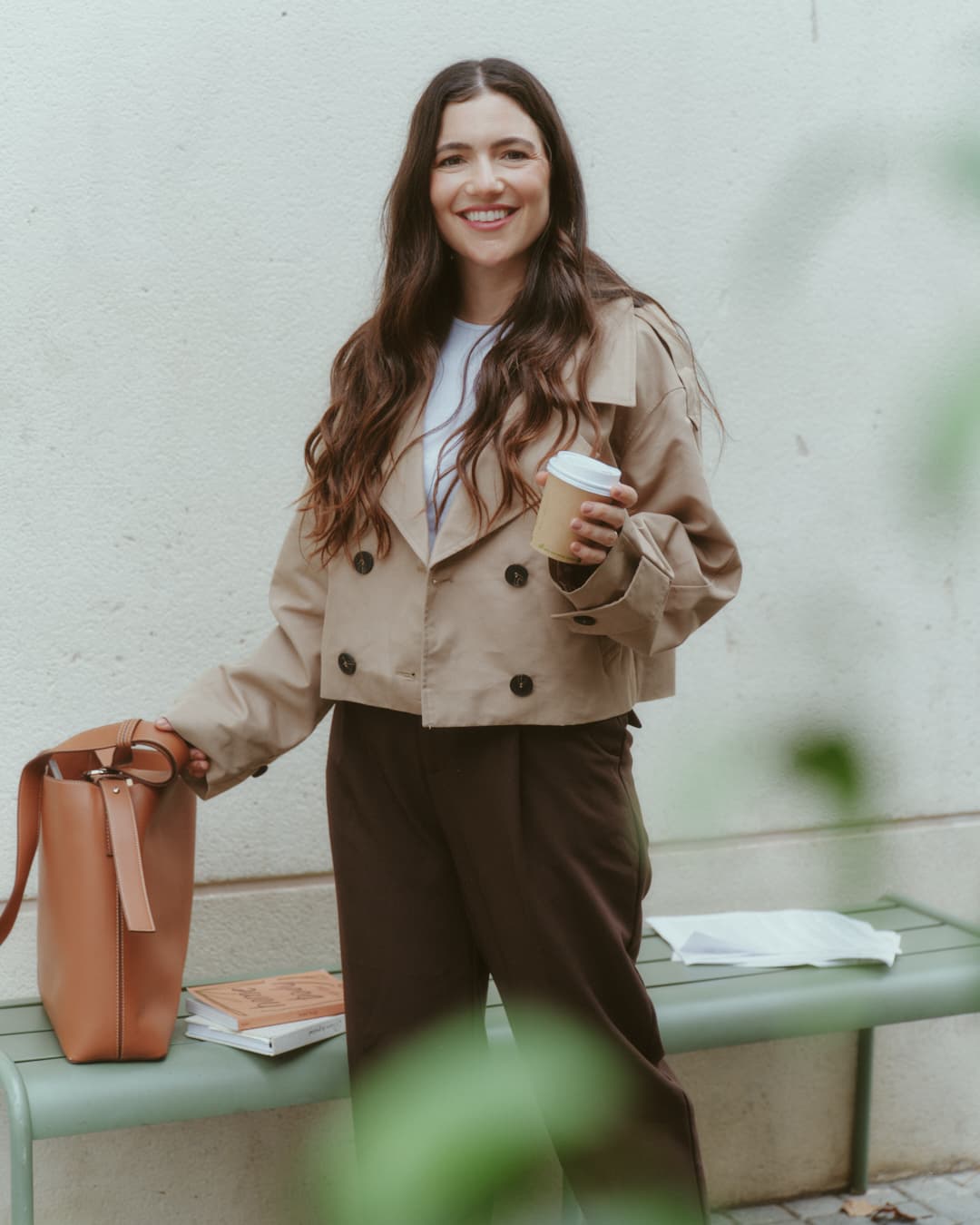 Guada holding a coffee, smiling next to a bench