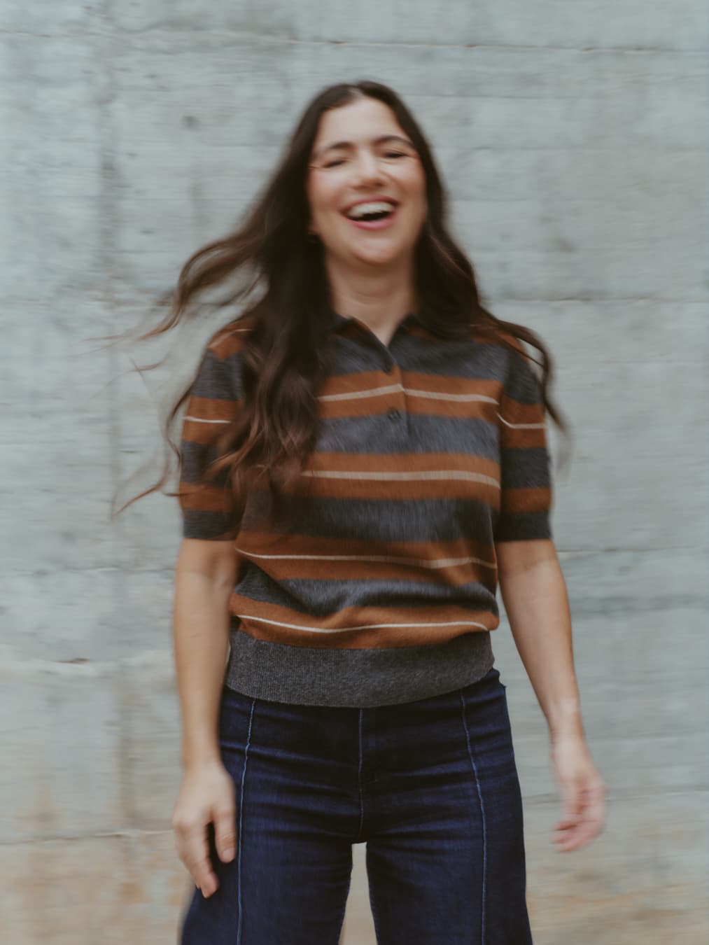 Guada laughing in front of a concrete wall, her hair in motion