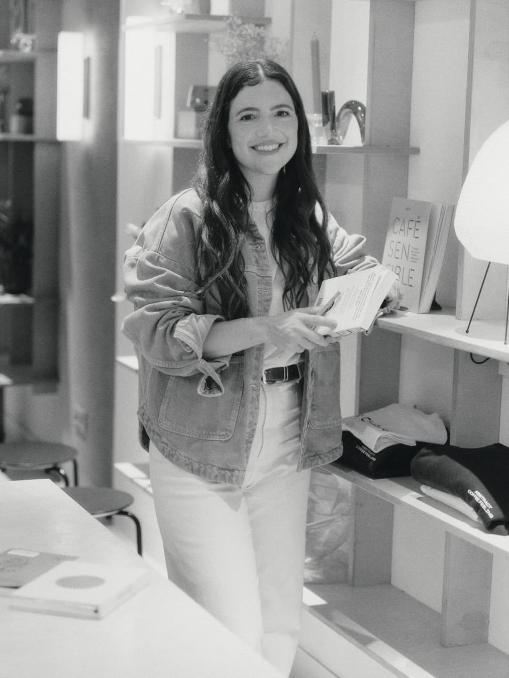 Guada smiling with a book in her hand, next to a bookshelf