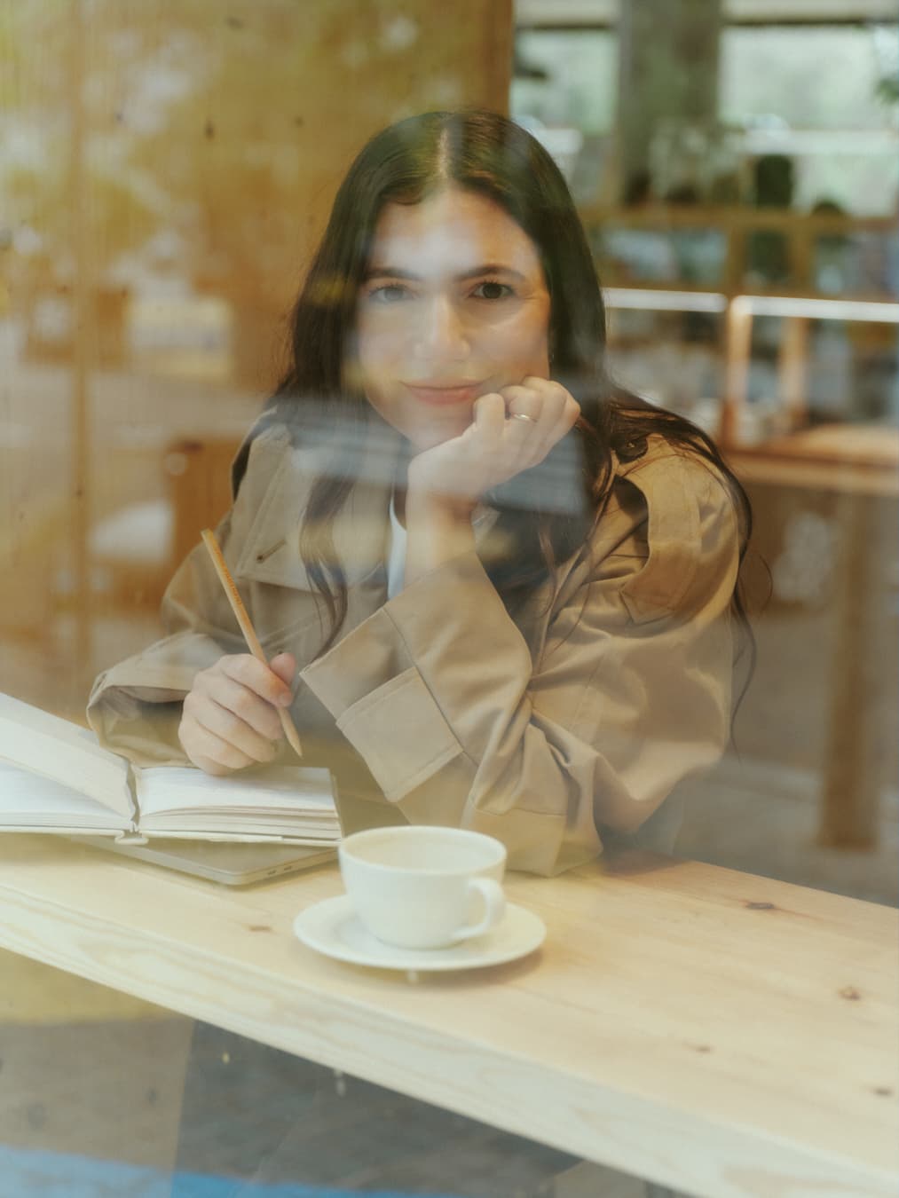 Guada behind a window with a coffee and a notebook, resting her chin on her hand