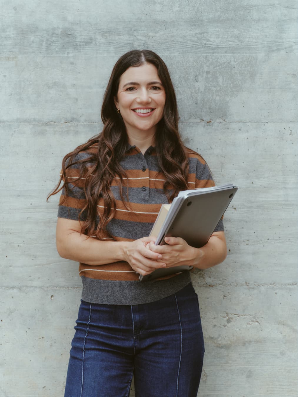 Guada sonriendo frente a una pared de hormigón, con una carpeta en las manos